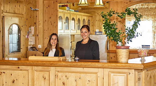 2 Empfangsdamen stehen hinter einer Rezeption aus Holz im Airport Hotel Fortuna